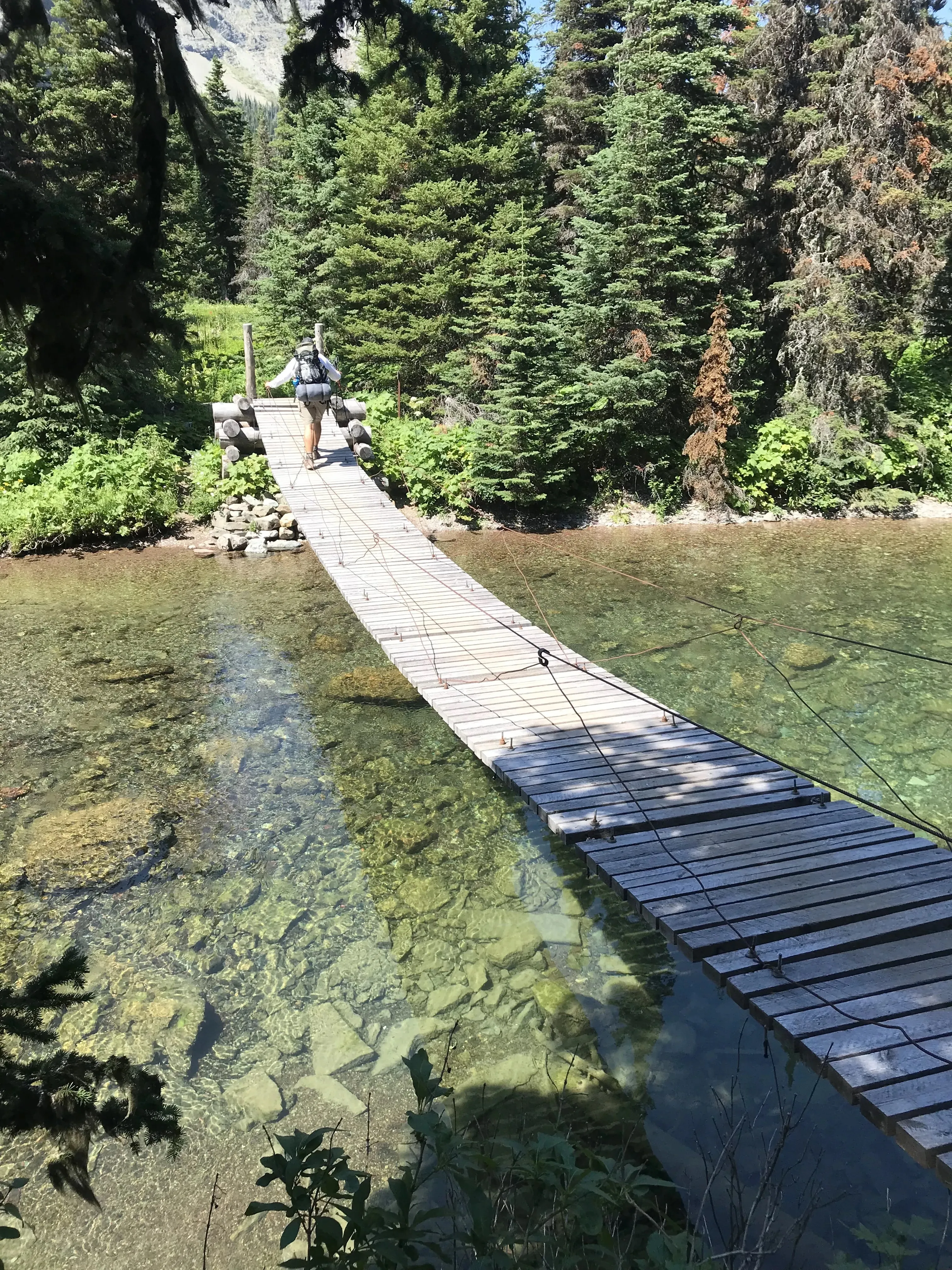 Backpacker crossing a wooden suspension bridge over a clear river