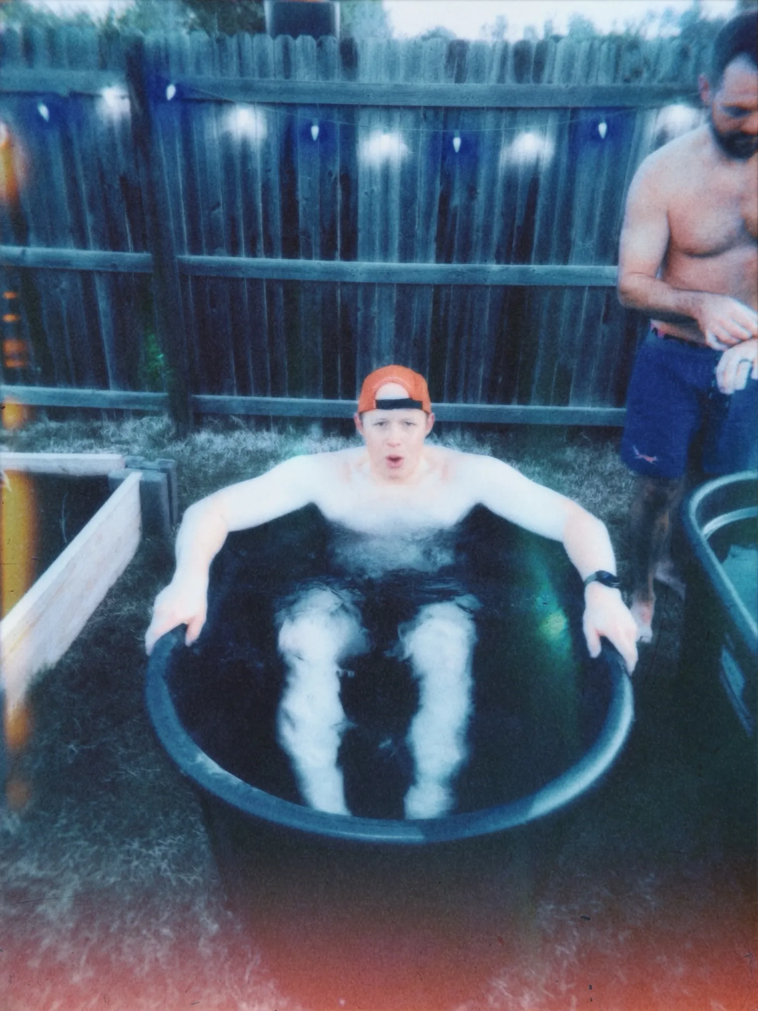 Man in an orange cap reacting in a cold plunge tub