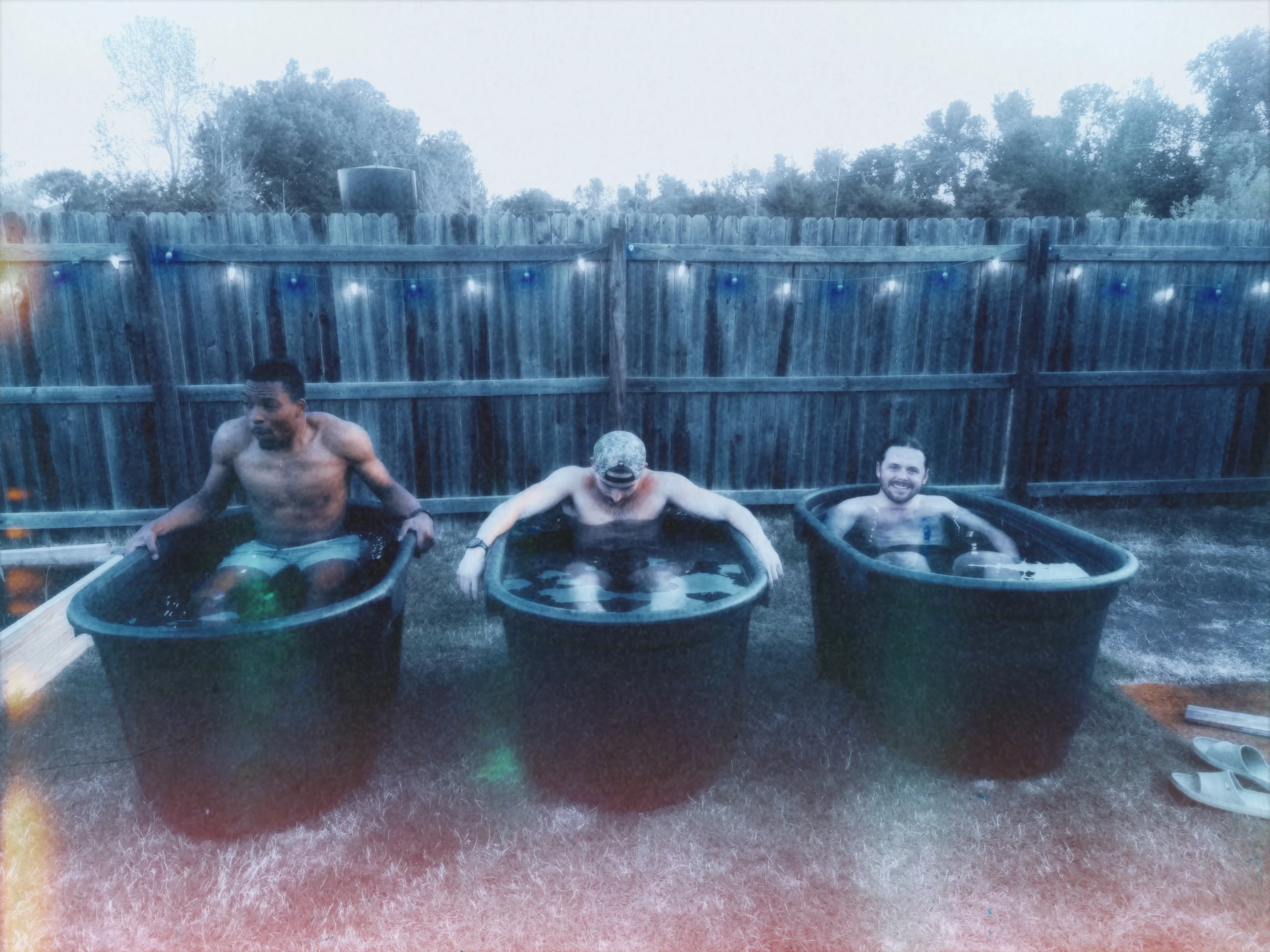 Three men cold plunging side by side under string lights
