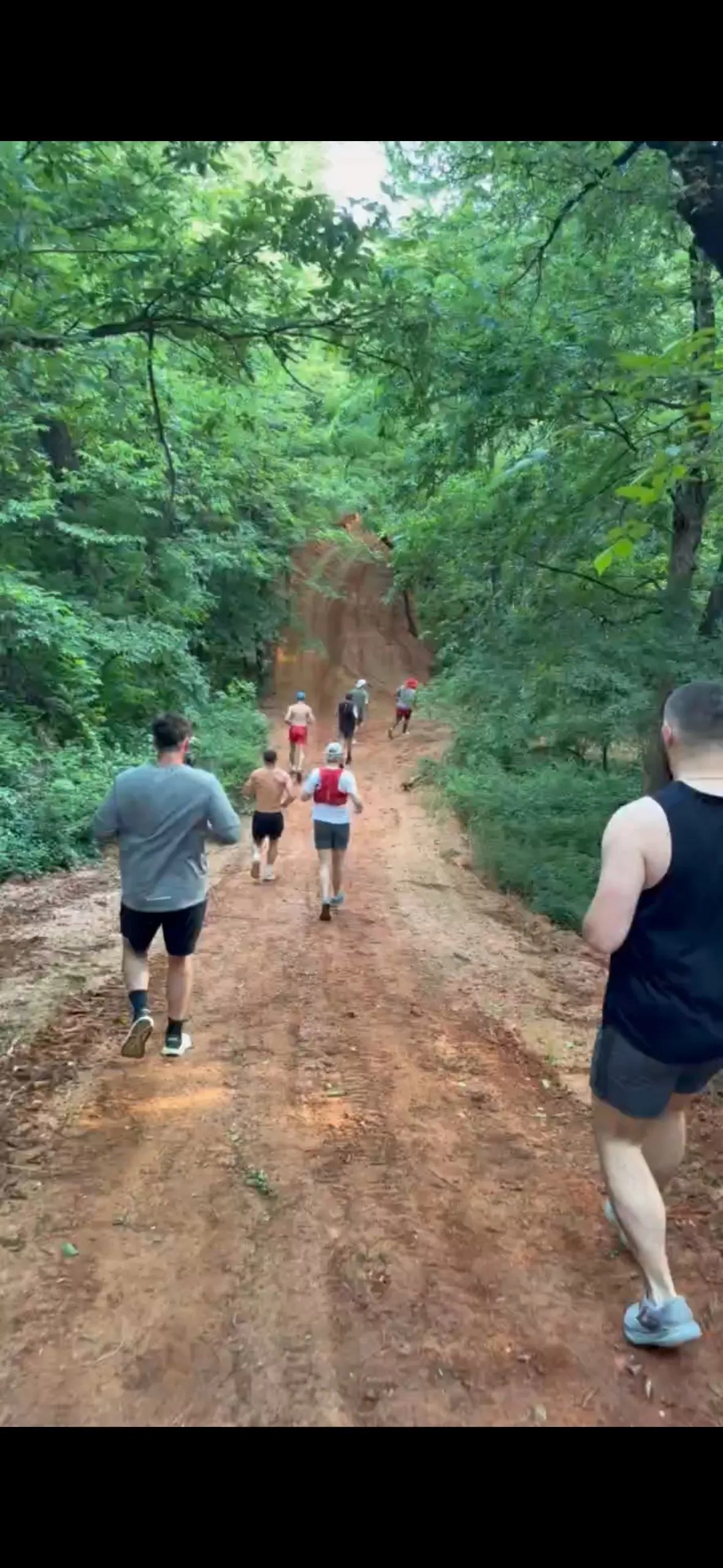 Runners climbing a red-dirt trail through the woods