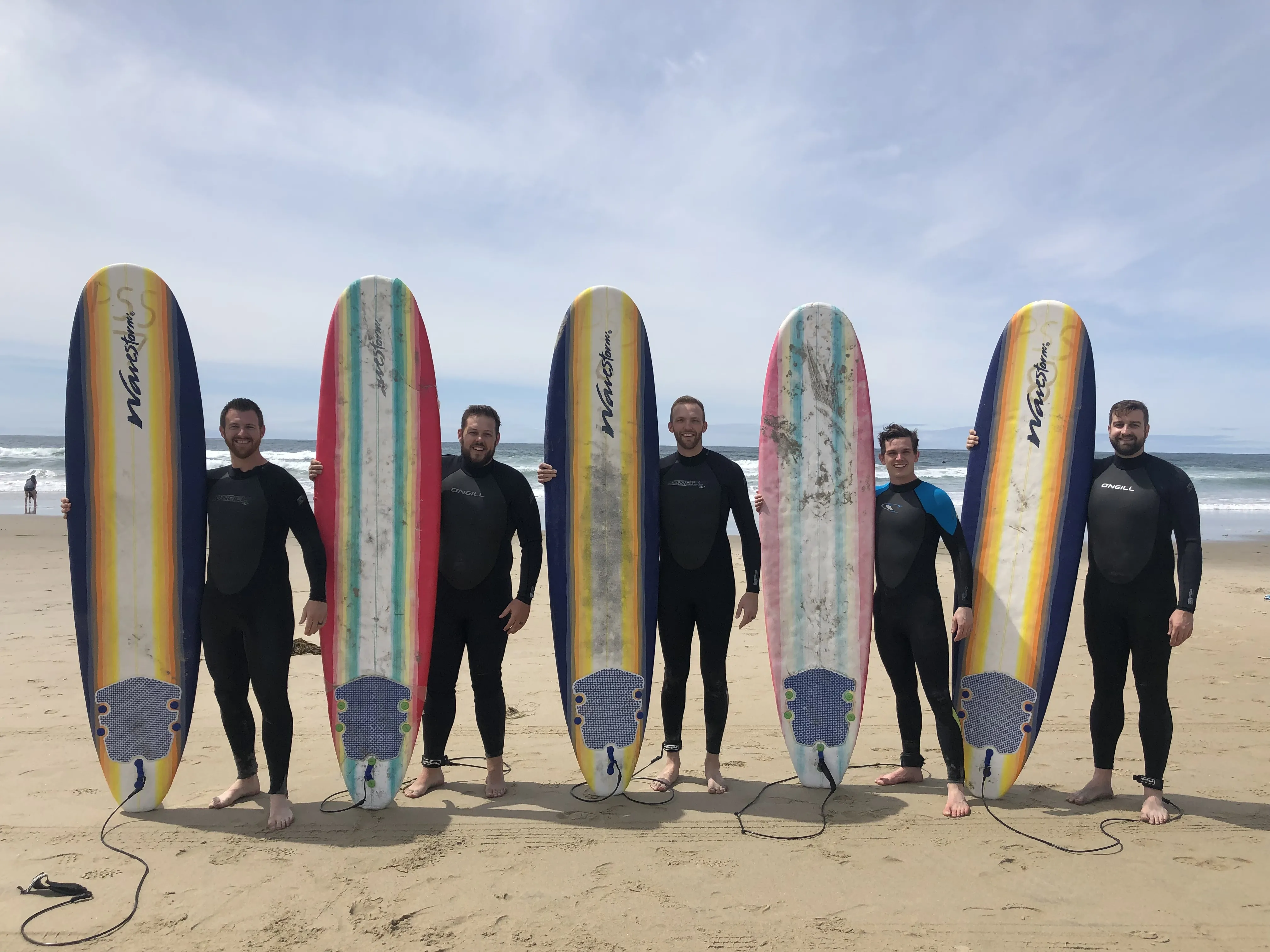 Five men in wetsuits with longboards on the beach by the ocean
