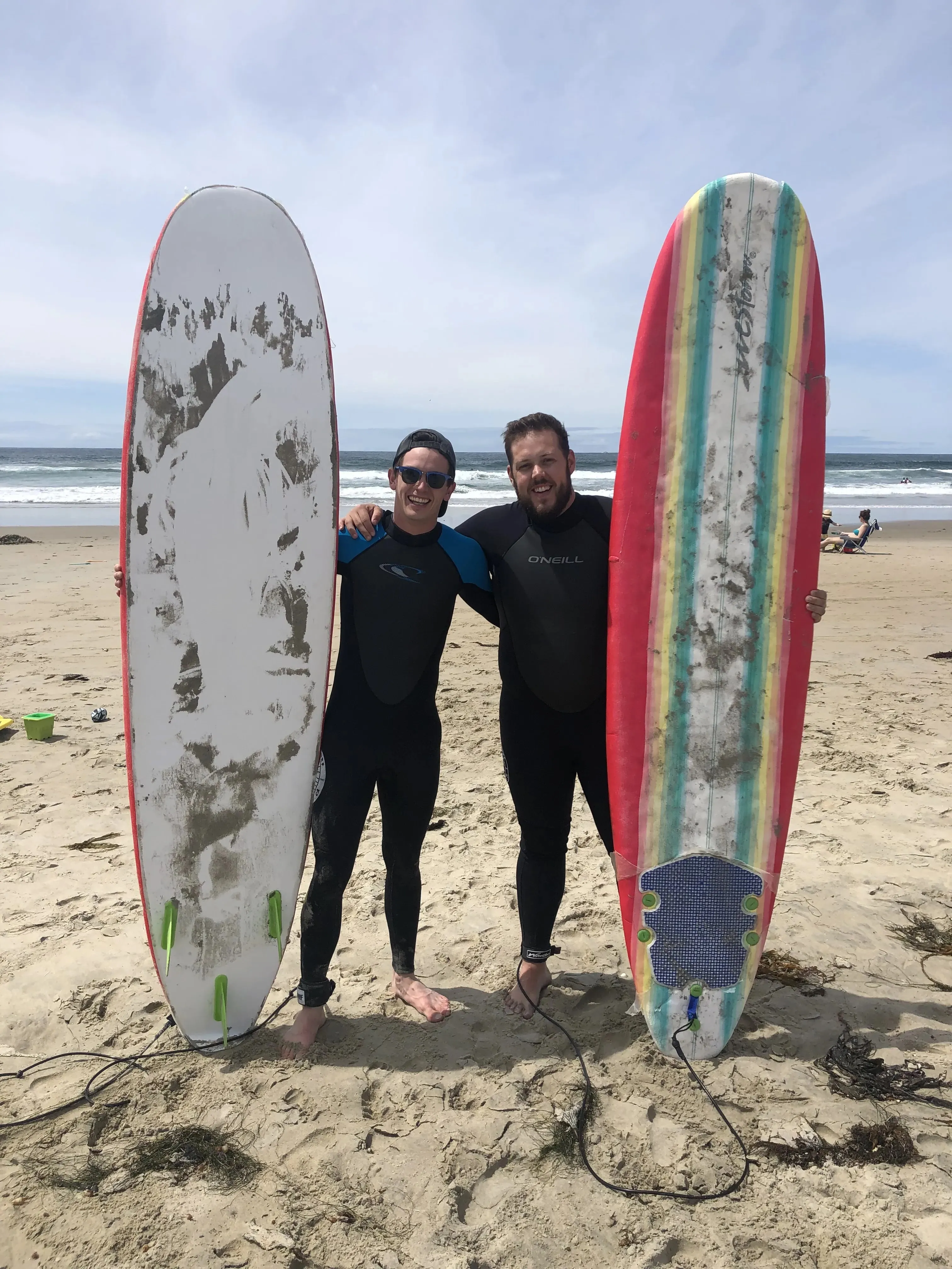 Two surfers in wetsuits holding boards on the sand